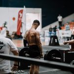 A weightlifting athlete prepares for a lift during a competition with judges observing.